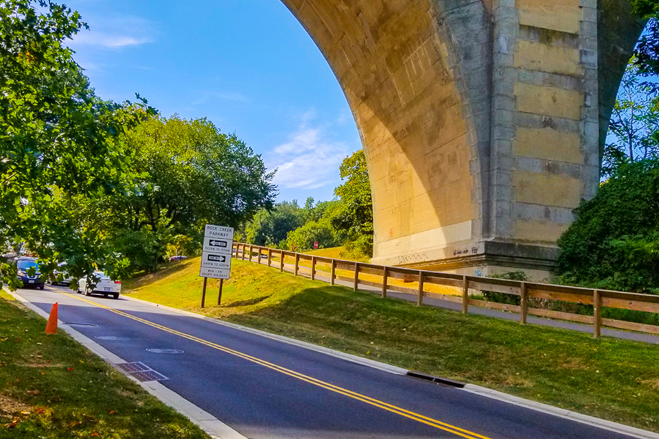 Connecticut Avenue Bridge over Beach Drive in Rock Creek Park. Road beneath bridge with nearby trail.