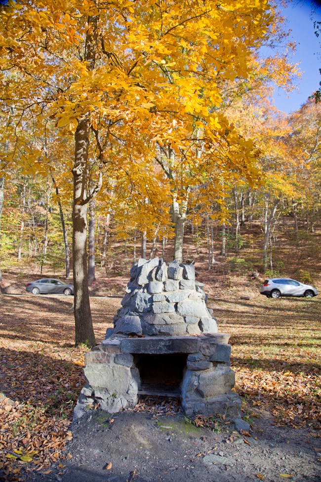 An old stone stove sits at one of the picnic grounds, with yellow leaves of autumn above it.