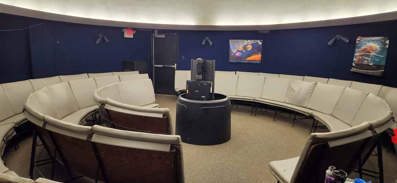 A room with dark blue walls, bright white domed ceiling and gray benches in a circle