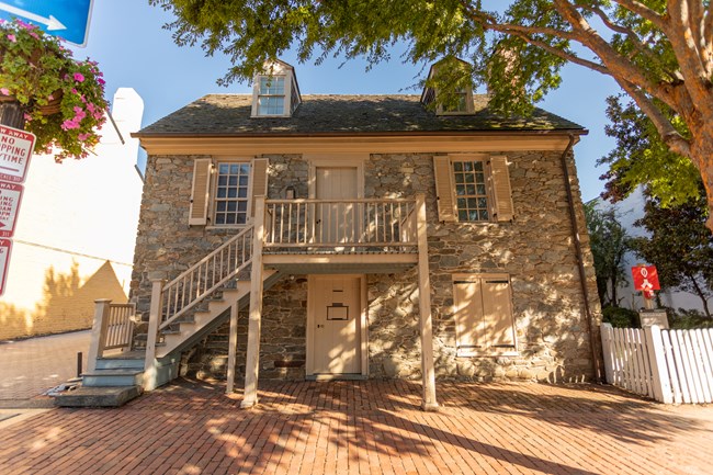 The front of a three-story stone building with a staircase up to a door in the middle of the second story, above a door on street level.