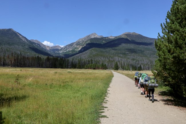 A group of three people are hiking down a trail, carrying overnight backpacking gear. They are heading on an overnight backpacking trip.