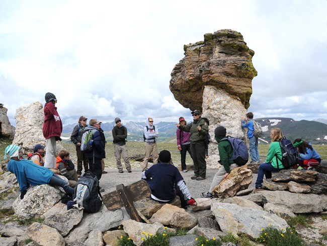 Students gather around a park ranger at the top of a mountain amidst light colored rocks.