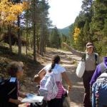 Students use a map along a trail with a ranger pointing to the adjacent forest.