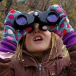 A student wearing colorful gloves looks up using binoculars.