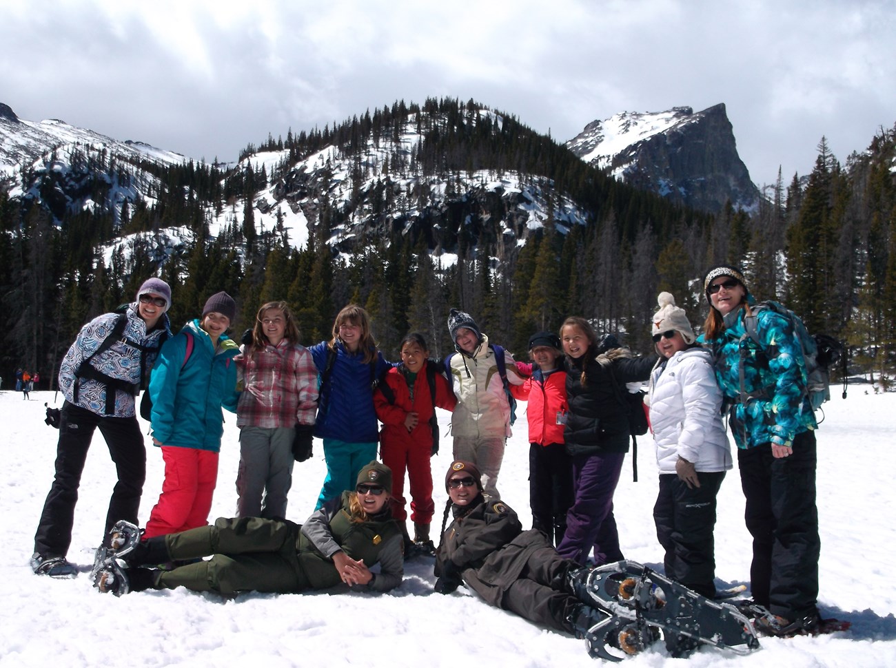 A group of girl scouts and 2 rangers standing on a frozen lake with mountains in the background