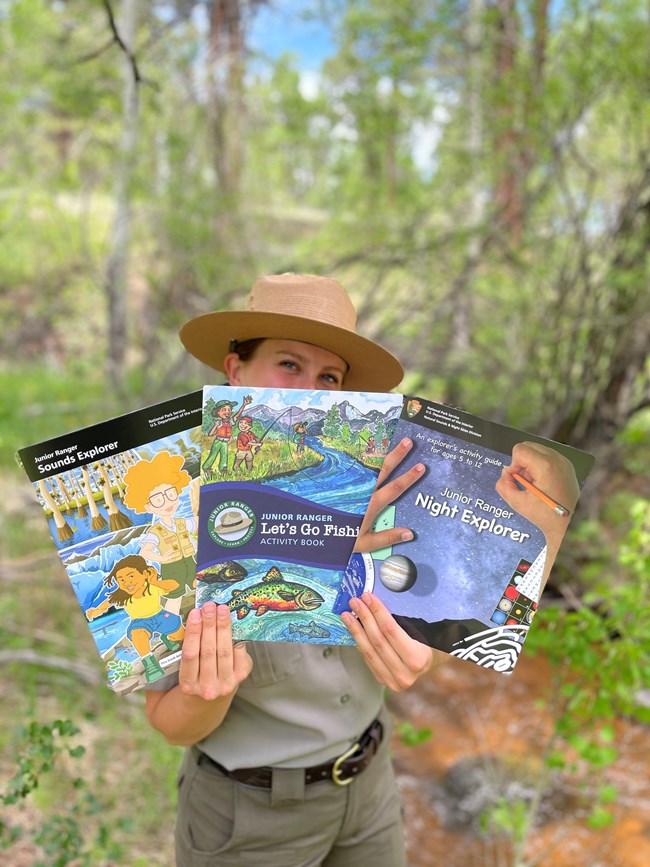 A park ranger is holding three different Junior Ranger Explorer Books