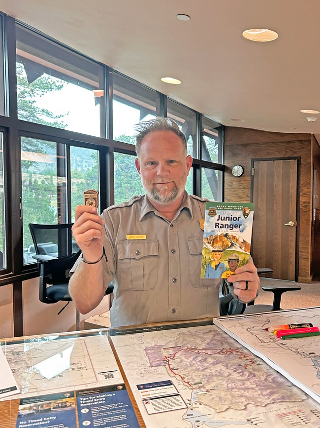 A park ranger is holding up a badge is his left hand and a book in his right.