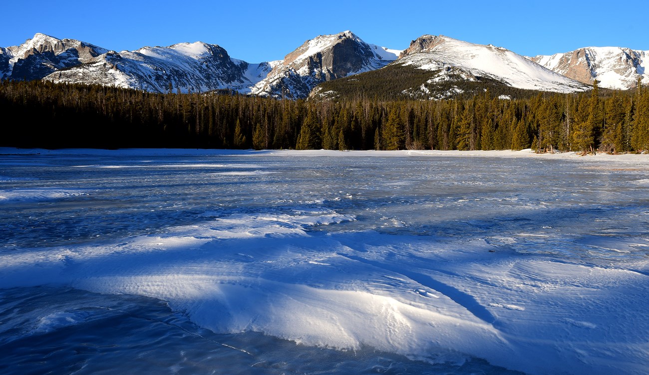 Bierstadt Lake with snow in winter on a clear, sunny day. Distant mountain peaks have snow on top.