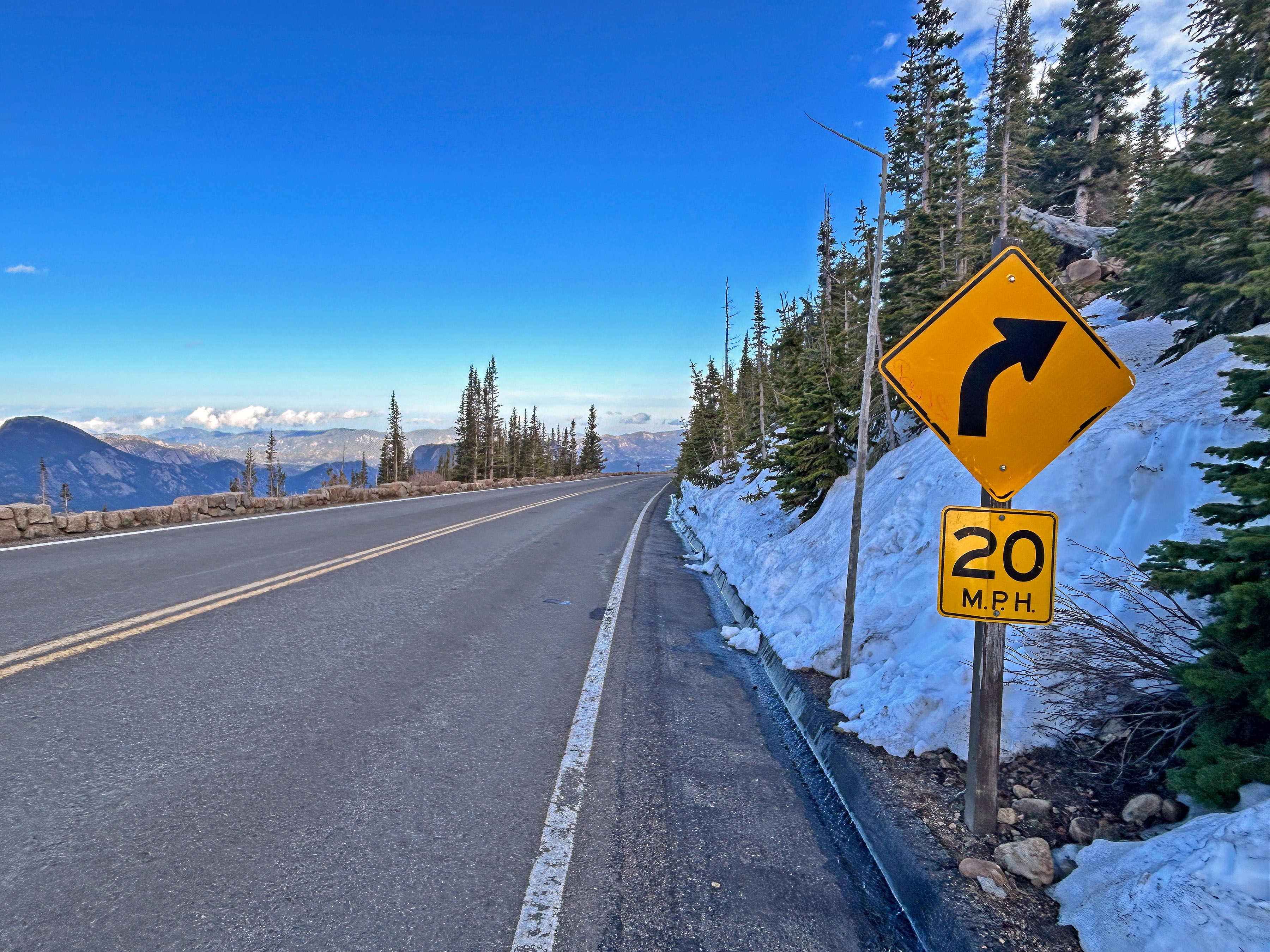 Section of Trail Ridge Road above Rainbow Curve, with scenic views of mountain peaks at sunset to the left of the road, off in the distance.