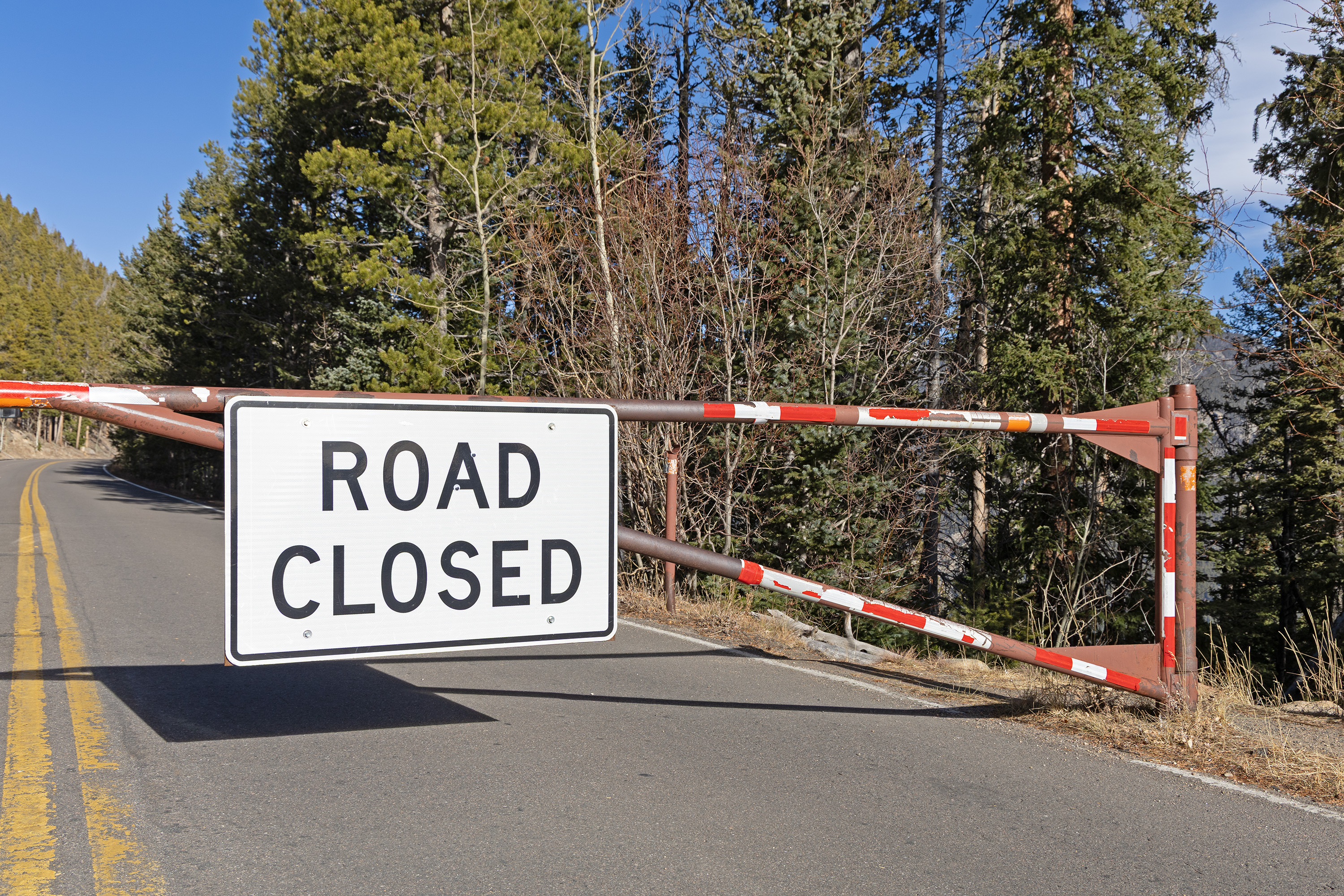 Road gate is closed on Trail Ridge Road at Many Parks Curve in RMNP. Large white road closed sign is posted on the center of the gate.