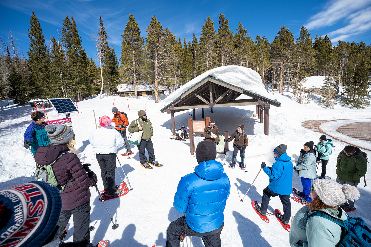 A group of park visitors are gathered around a park ranger, ready to begin a snowshoe walk