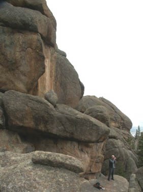 Photo hiker standing in front of massive rock formation along trail.