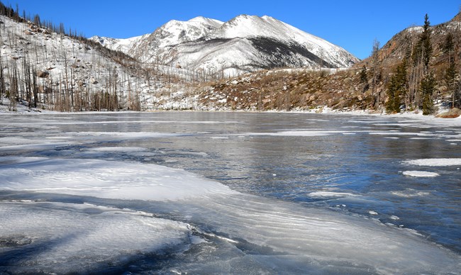 Cub Lake is frozen with snow on mountain peaks in the distance
