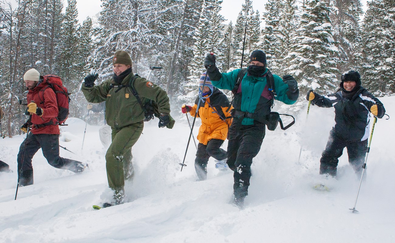 Five visitors and a ranger run through snow in snowshoes