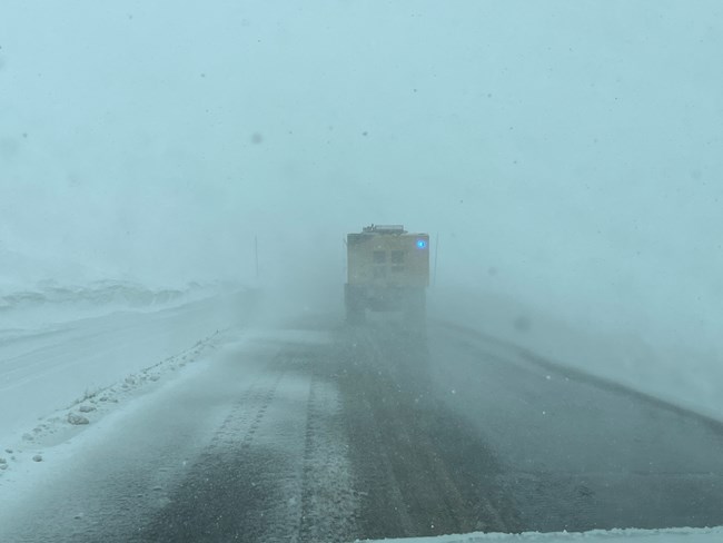 A snowplow is working on Trail Ridge Road. It is snowing with poor visibility and dark clouds.