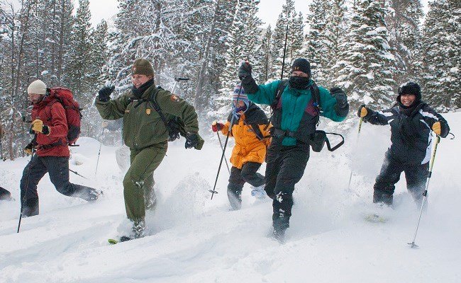 A group of park visitors are snowshoeing with a park ranger