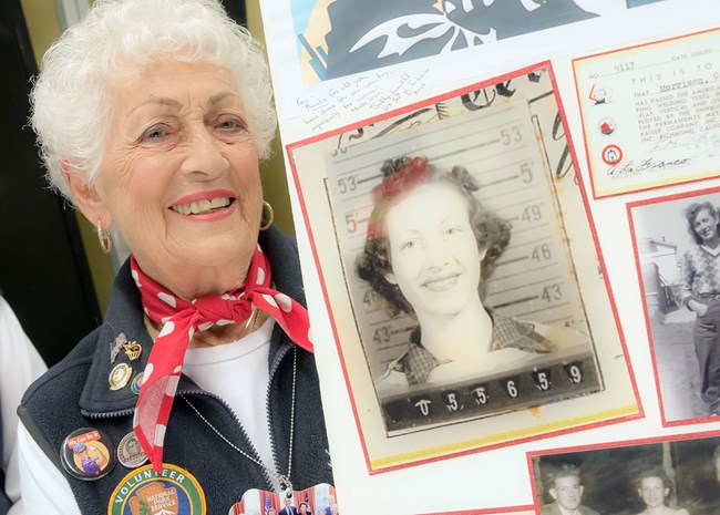 Senior caucasian female smiles at the camera while holding a board with a photo of her younger self.