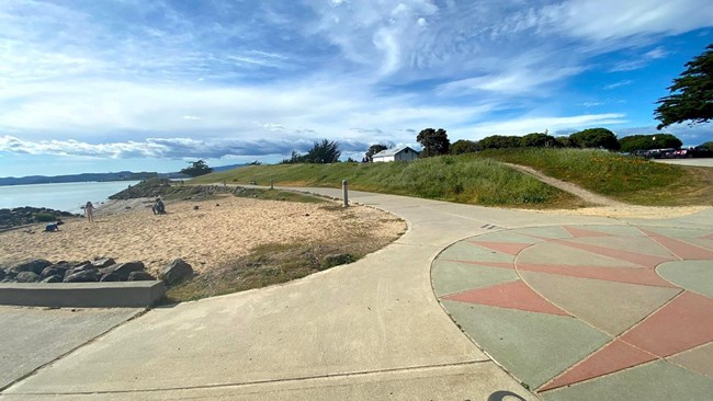 Park pathways surrounded by sand and grass. Bay is visible.