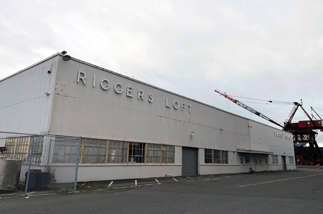 Historic warehouse building sitting on concrete dock. Crane can be seen in the background.