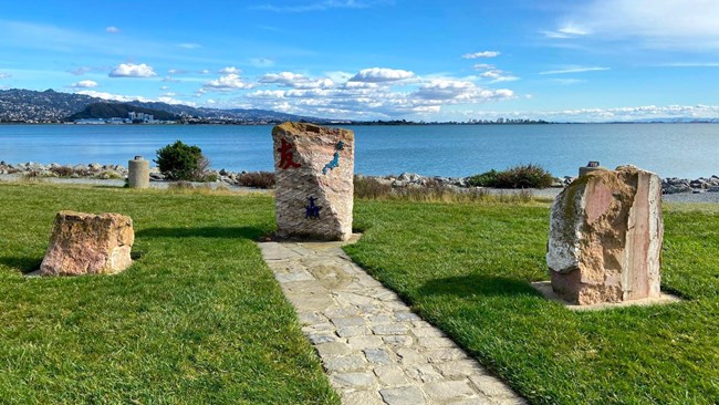 Stone pathway leads to three stones. Bay view in distance.