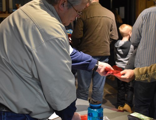 A volunteer hands red cellophane to a visitor over a desk.