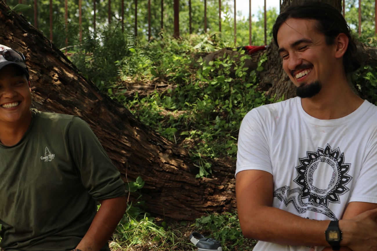 Two members of a volunteer work crew, one male and one female, sit on a concrete wall and smile.