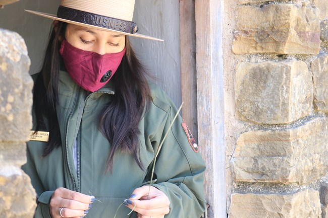 Female Park Ranger wearing mask holds a native plant fiber used for thread.