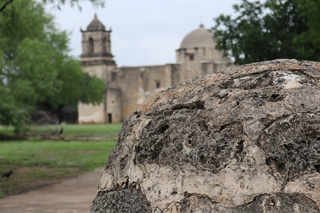 Reconstructed limestone horno dome in foreground with limestone Mission San Jose church in background.