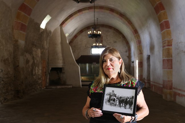 Woman standing inside a granary holding a picture of her ancestor.