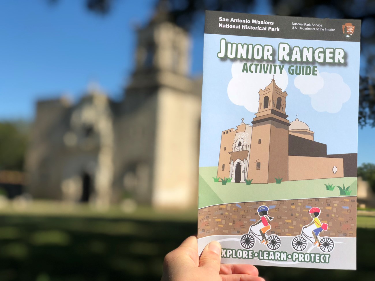 Junior Ranger booklet being held up in front of the church at Mission San Jose