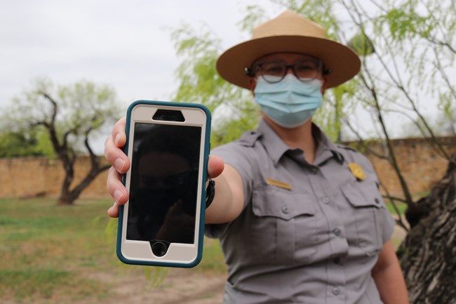 A park ranger standing in the background holds up a cell phone in the foreground.