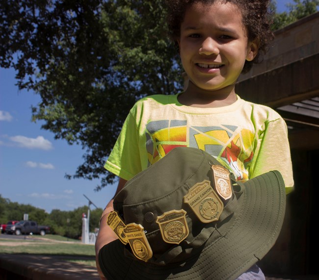 Junior Ranger holds up the badges he's earned at various National Parks.