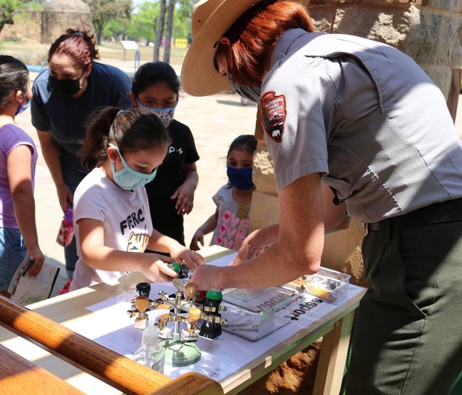 Group of young junior rangers stamp their junior ranger activity book with cancellation stamps. Park Ranger assists.