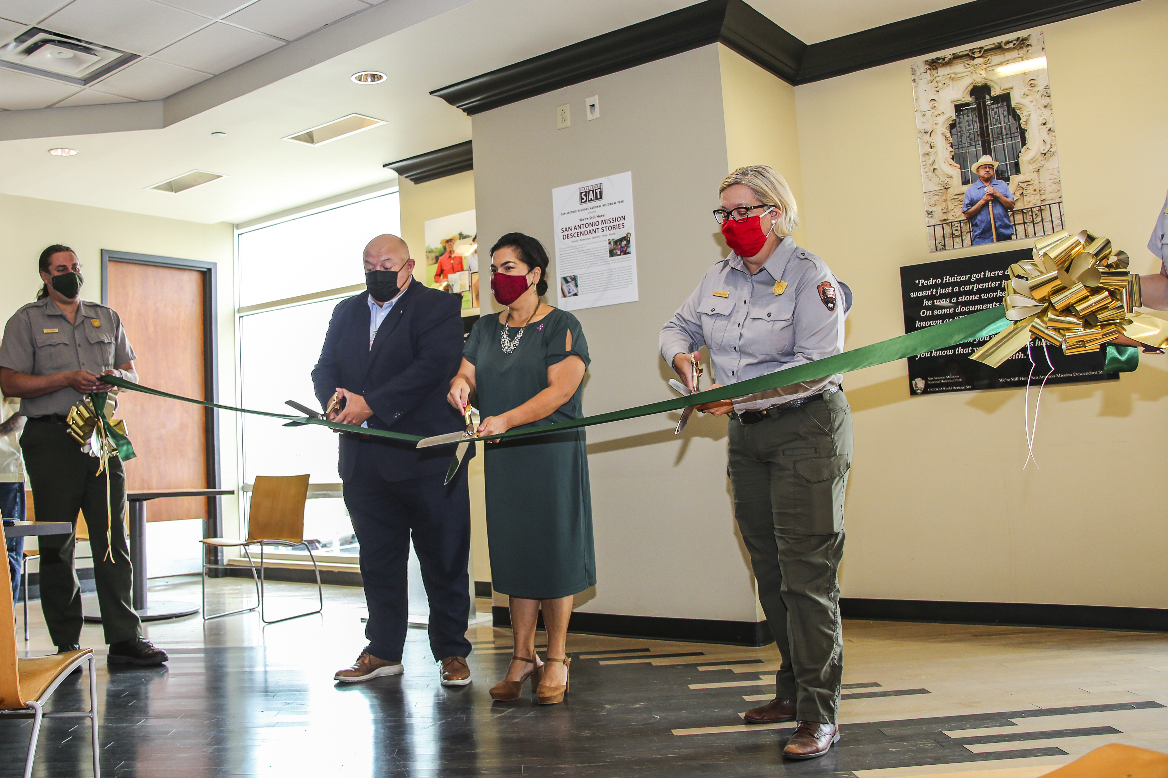 Three officials cutting a large ribbon.