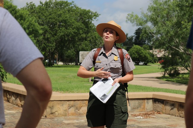 Female park ranger speaks to visitors while standing outside and holding a historic map