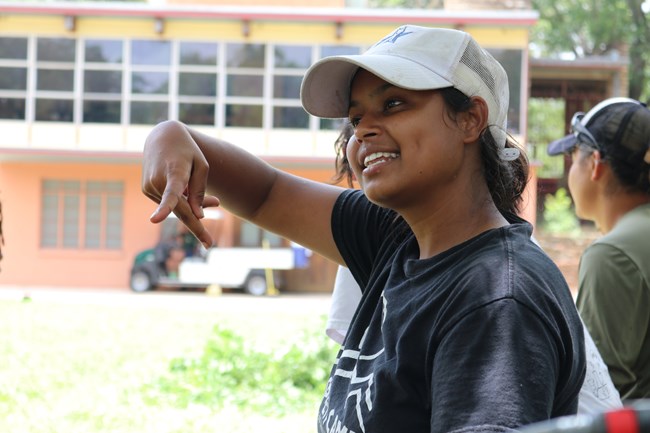 Young woman signs the letter K while smiling and looking past the camera.