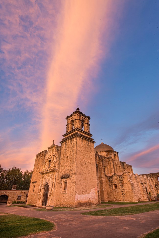 Mission San Jose church and convento buildings against a pink sunset