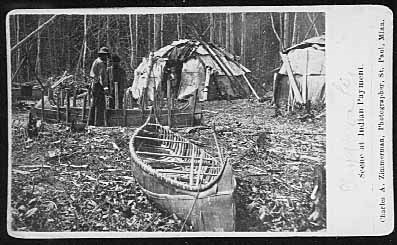 Canoe in frame being built with wigwams in background