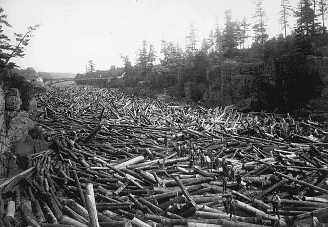 Logs fill the river as far as the eye can see, while men stand on the logs