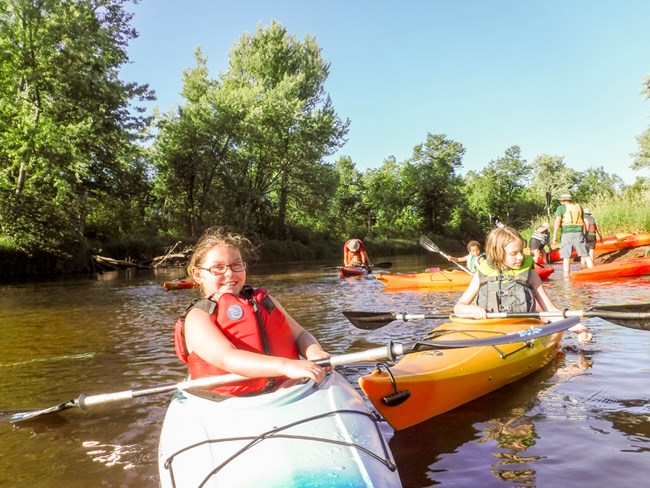 Kids sit in kayaks on a river