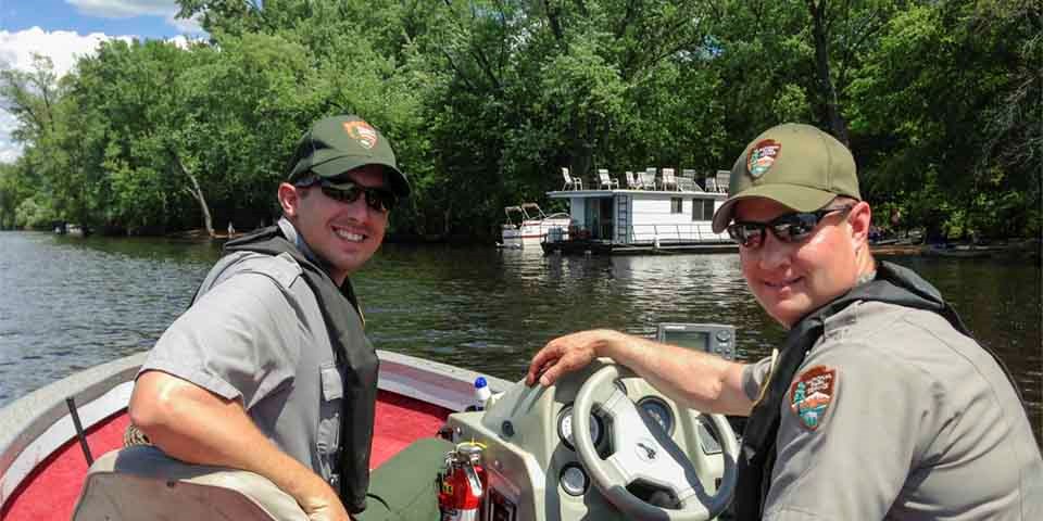 Two park rangers smile from a boat. Two park rangers smile from a boat.