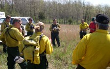 Men and women dressed in fire resistant yllow shirts and green pants gathe round the burn boss