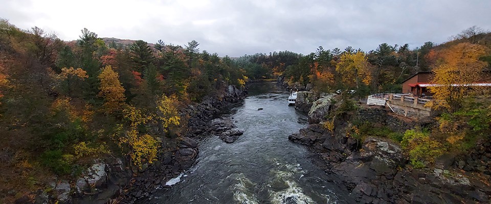 A swift-moving river moves through a basalt gorge of rock under an overcast sky.