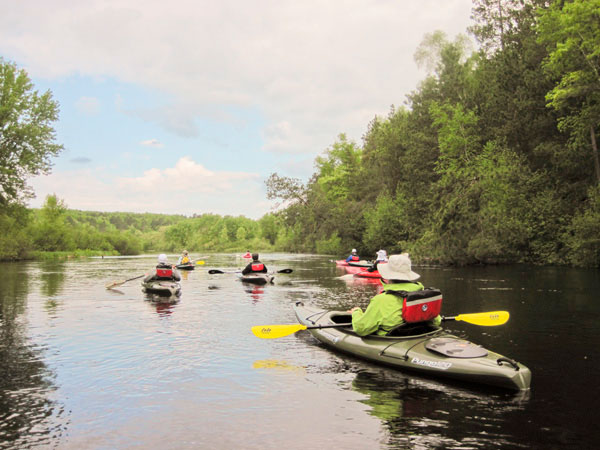 Group of kayakers wearing hats and jacketspaddle downriver on cool summer day with clouds