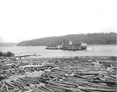 A steamer on a busy river with floating logs in the foreground.