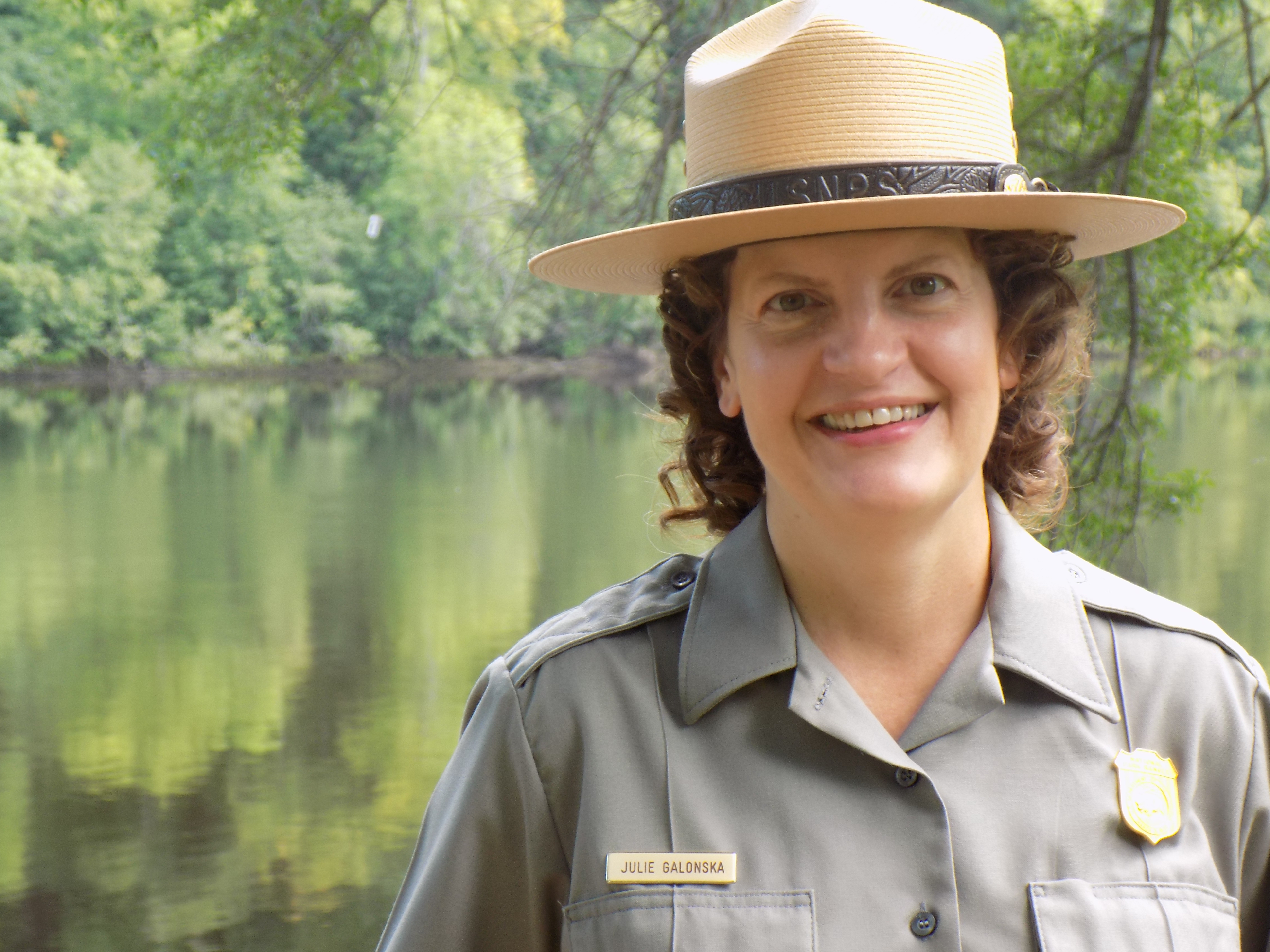 A female park ranger stands next to water.