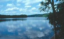 wide river with white clouds in blue sky reflected in water