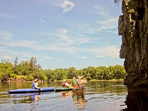 People in kayaks point towards a tall cliff.