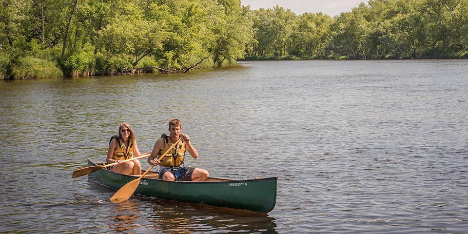 Canoes on the St. Croix Two canoers paddle on a river through a forested landscape.