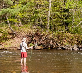 A man stands in a river with a fishing pole.